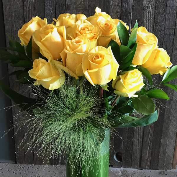 Yellow roses arranged in a tall green vase with grassy filler