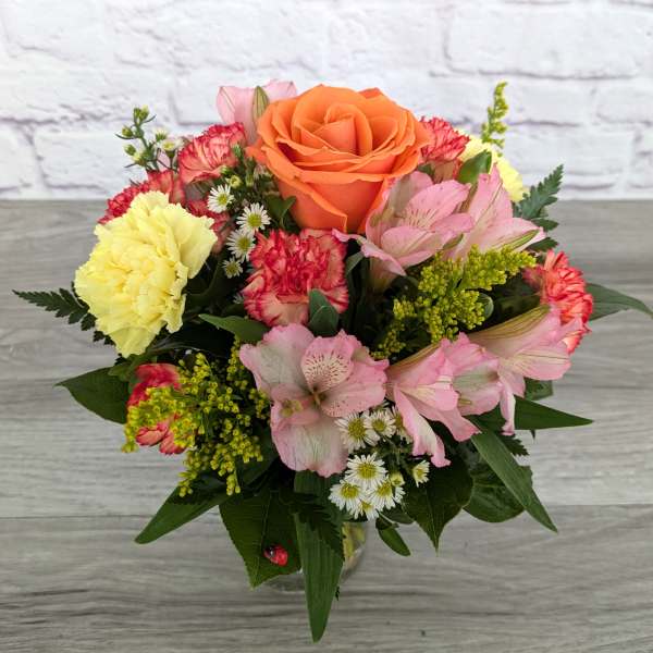 Mixed bouquet with an orange rose, pink lilies, and yellow carnations in a vase