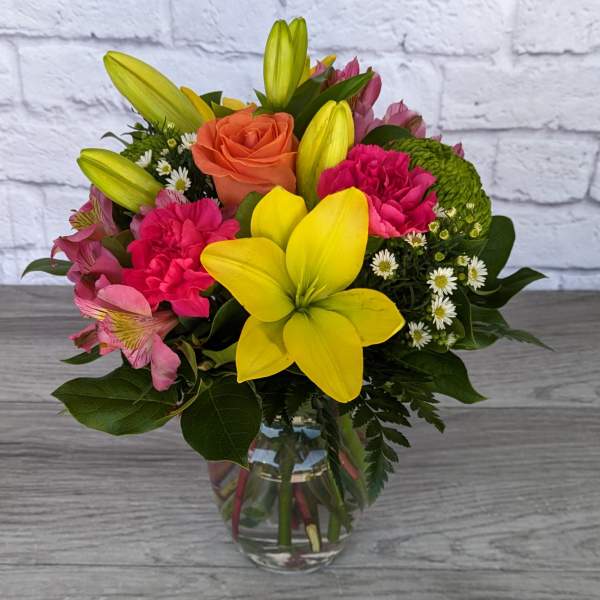 Mixed bouquet with yellow lilies, pink carnations, and an orange rose in a glass vase.
