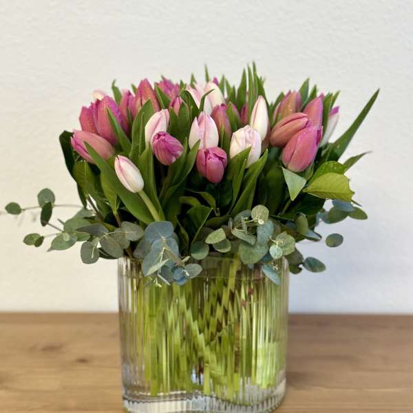 Pink tulips arranged in a clear glass vase with eucalyptus