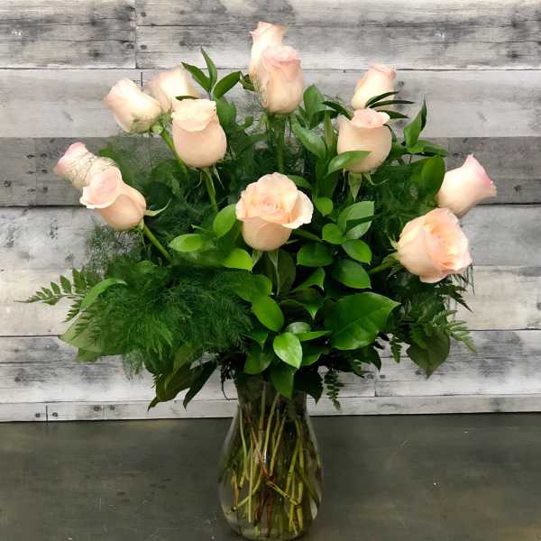 Pale pink roses arranged in a clear glass vase with lush greenery