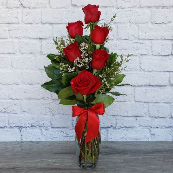 Red roses arranged in a clear glass vase with a red ribbon
