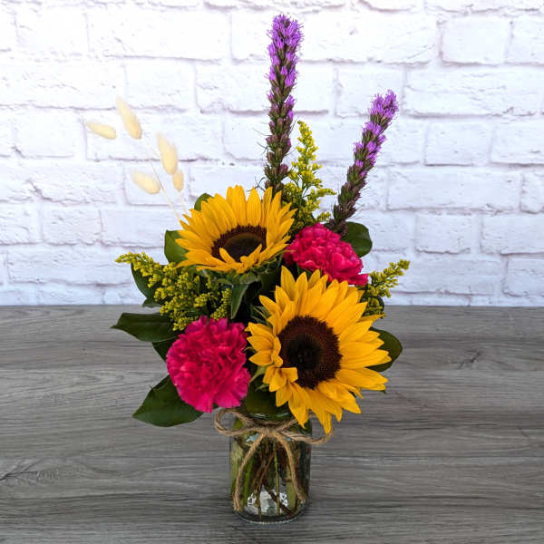 Sunflowers and pink carnations in a glass vase with dried accents