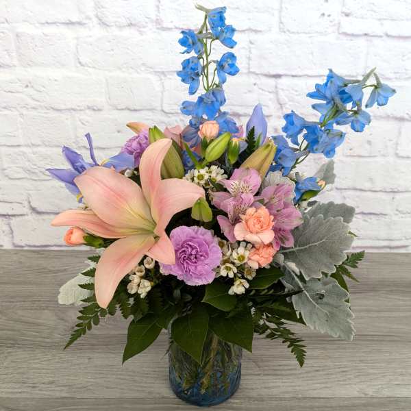 Pastel bouquet with pink lilies and blue delphinium in a glass vase