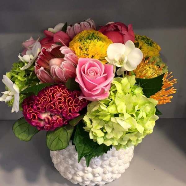 Mixed bouquet with pink rose, orchids, hydrangea, and yellow blooms in a white vase