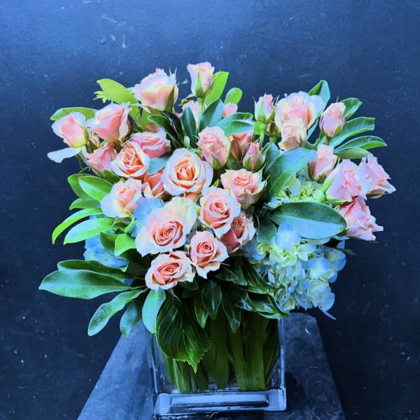 Peach roses and blue hydrangeas in a clear square vase