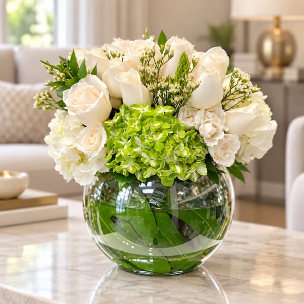 White roses and hydrangeas arranged in a round glass vase