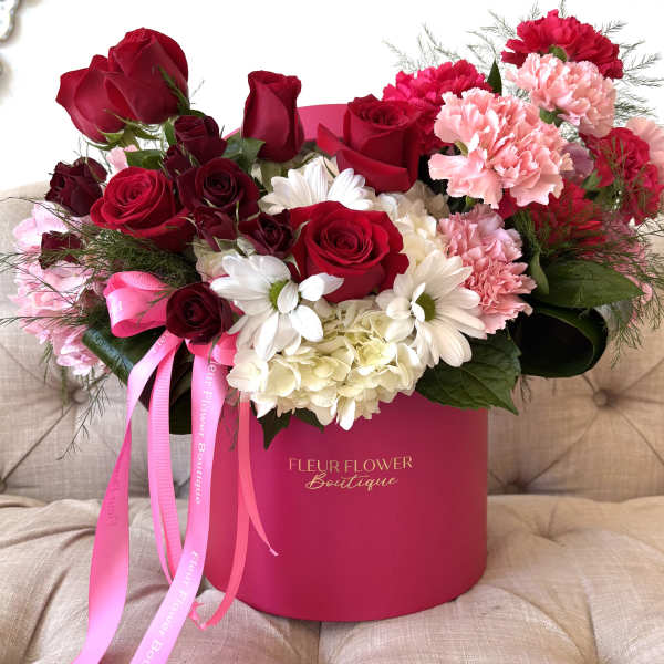 Red roses and pink carnations in a pink hatbox with ribbon