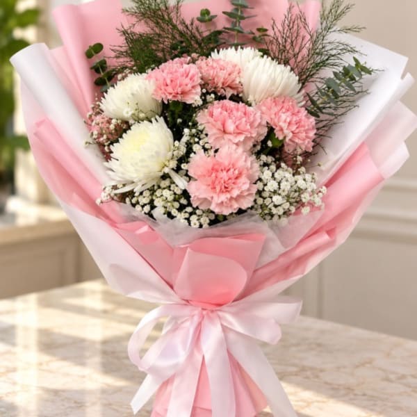Pink and white bouquet of carnations and small white filler flowers wrapped in pink paper