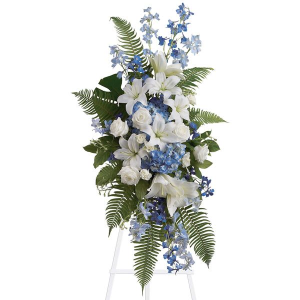 Tall white and blue floral spray with lilies and roses on a clear stand