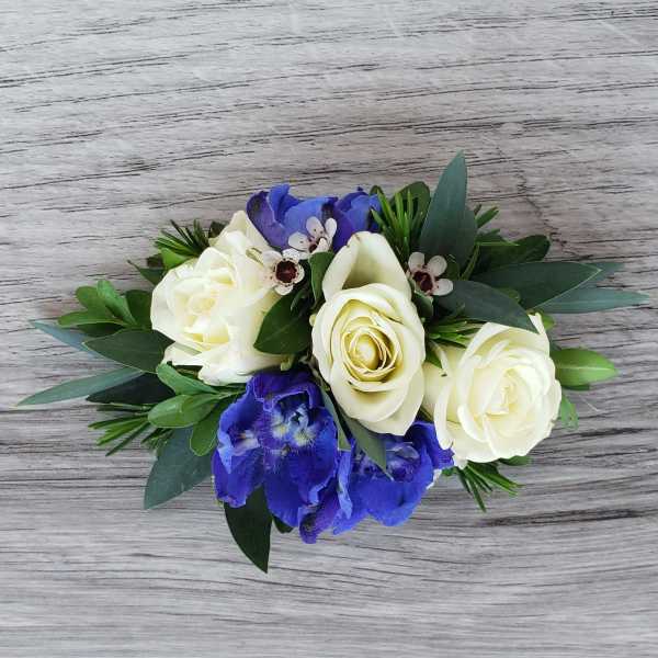 White roses and blue flowers arranged with greenery on a wood surface