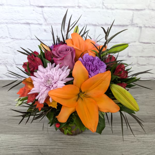 Orange lilies and purple flowers in a low vase arrangement