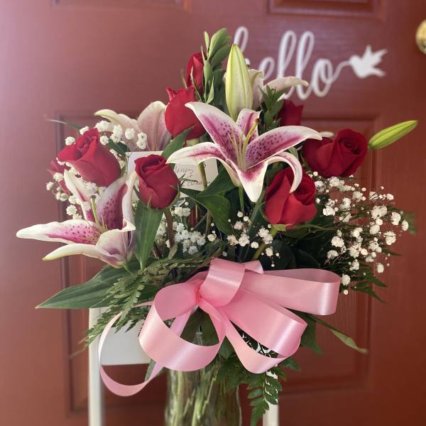 Bouquet of red roses and pink lilies in a glass vase with a pink ribbon