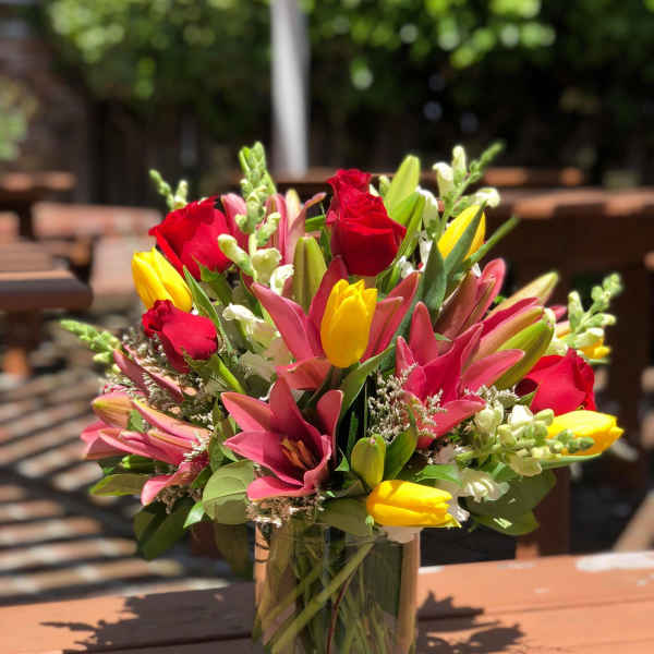 Mixed bouquet of red roses, pink lilies, and yellow tulips in a glass vase