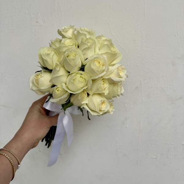 Handheld bouquet of cream white roses tied with a white ribbon
