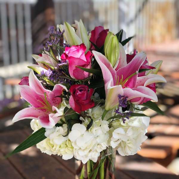 Pink lilies and roses in a clear glass vase with white hydrangeas