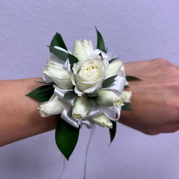 White rose wrist corsage with ribbon and dark green leaves