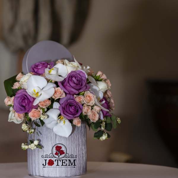 Bouquet of purple roses, white orchids, and peach spray roses in a gray box