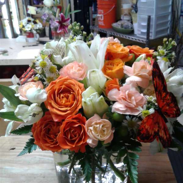 Orange and peach rose bouquet in a clear glass vase with white lilies