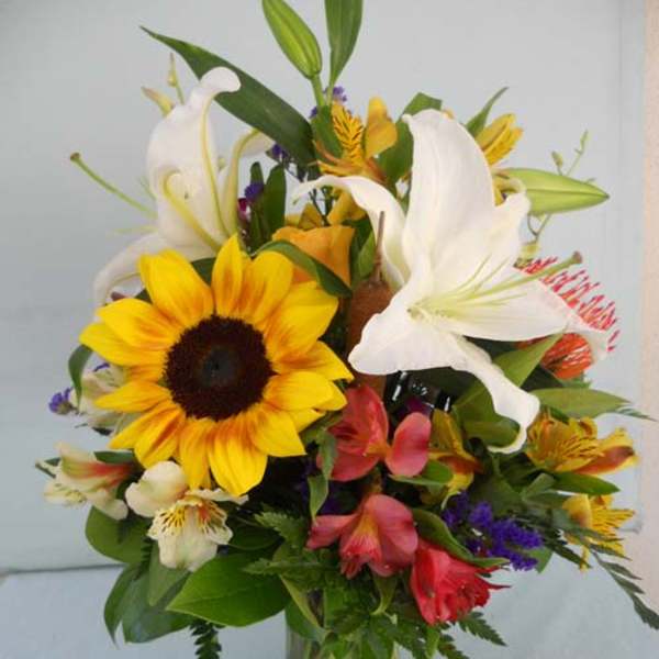 Mixed bouquet with sunflowers, white lilies, and colorful blooms in a glass vase