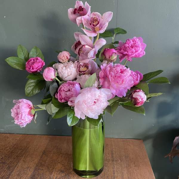 Pink peonies and orchids arranged in a green glass vase