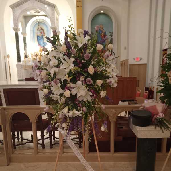Large standing floral spray with white lilies and purple flowers on an easel