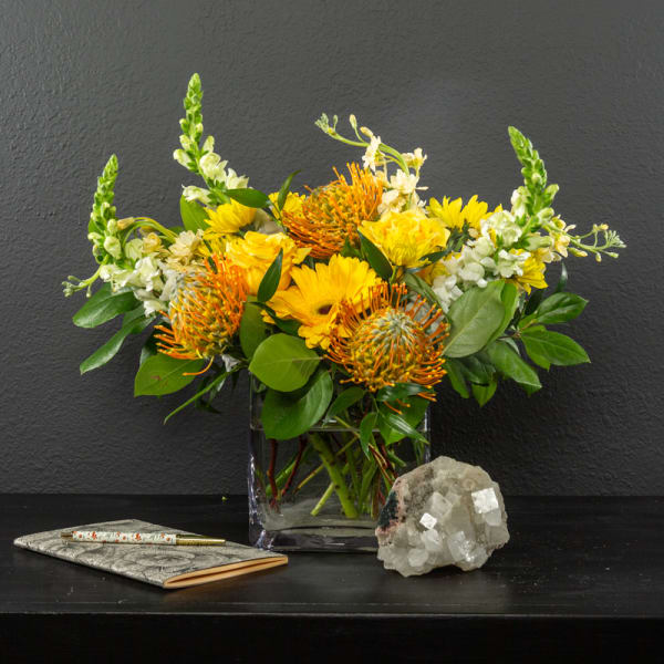 Yellow floral arrangement in a clear glass vase with a notebook and crystal