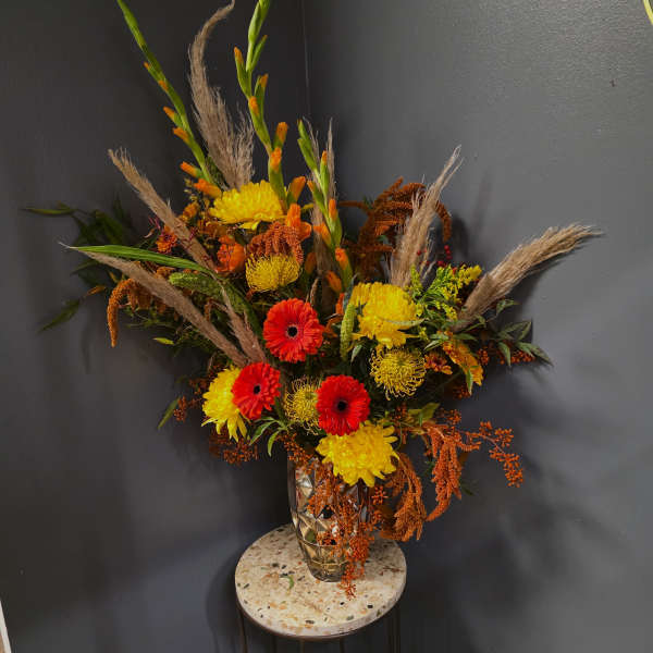 Tall autumn bouquet with red and yellow flowers in a glass vase