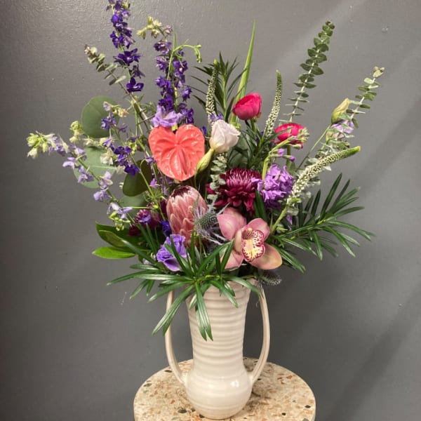 Tall mixed flower arrangement in a white handled vase with pink and purple blooms