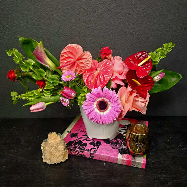 Pink and red floral arrangement in a white vase with a candle holder