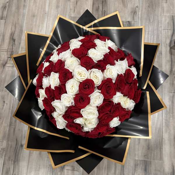 Round bouquet of red and white roses wrapped in black paper with gold trim