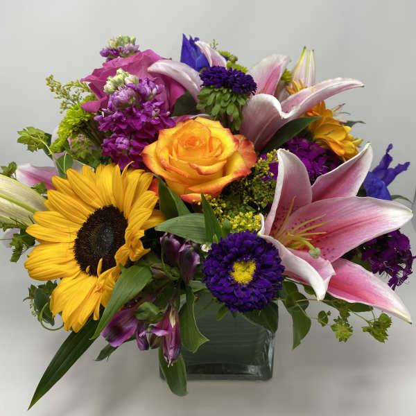 Mixed bouquet with sunflowers, pink lilies, and an orange rose in a glass vase