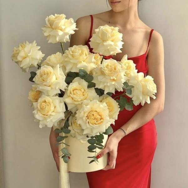 Woman in a red dress holding a cream rose arrangement in a box