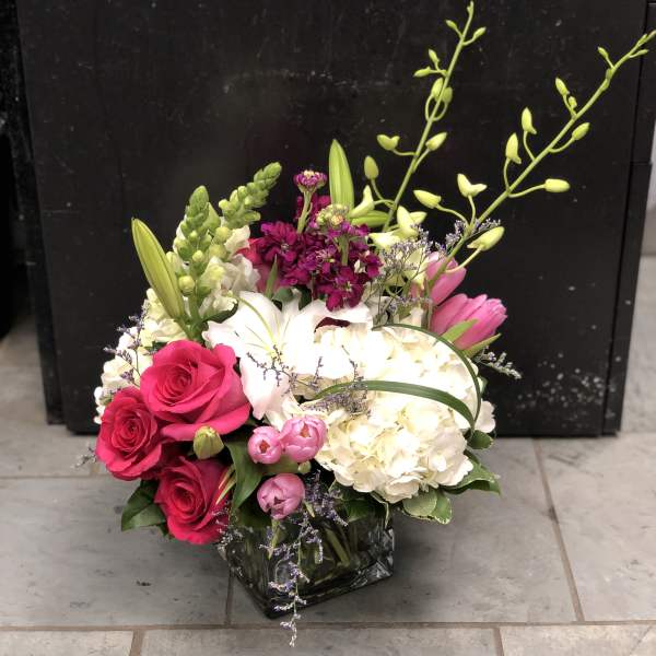 Pink roses and white lilies in a glass vase with hydrangea and orchids