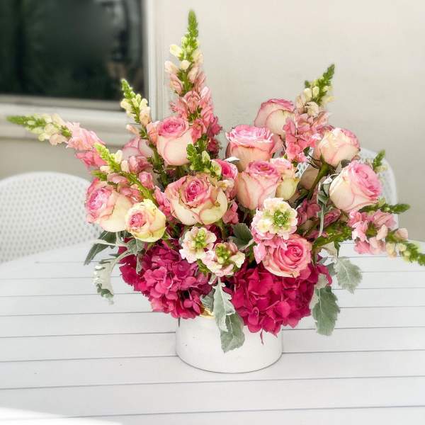 Pink and cream roses with tall snapdragons in a white vase
