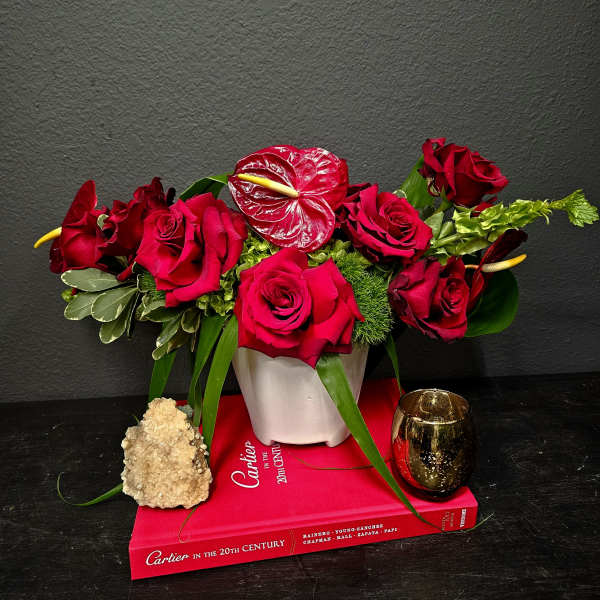 Red rose arrangement in a white vase with a gold candle and crystal accent