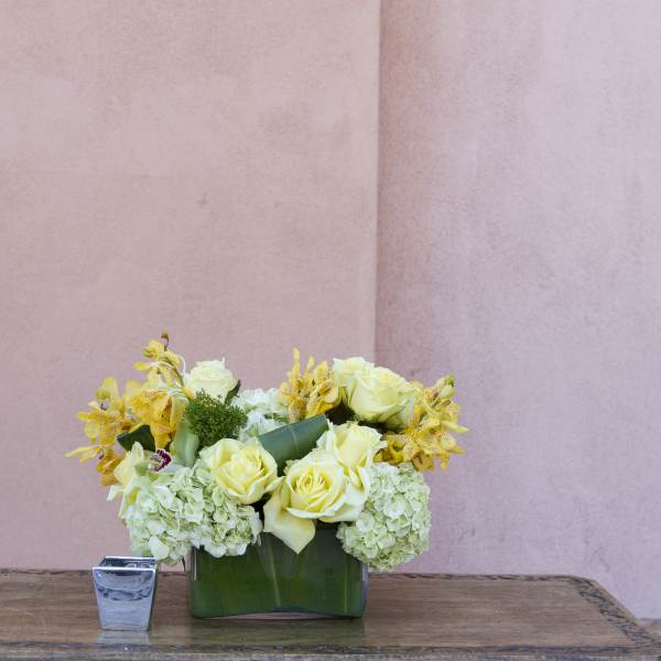 Yellow roses and pale hydrangeas arranged in a green vase