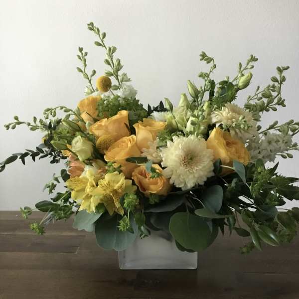 Yellow and white floral arrangement in a clear square vase