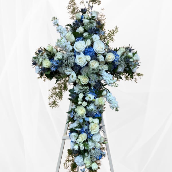 Large floral cross arrangement with white and blue flowers on a stand