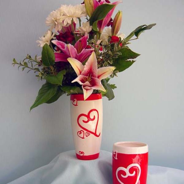 Pink lilies and white daisies in a tall heart-decorated vase with a matching cup