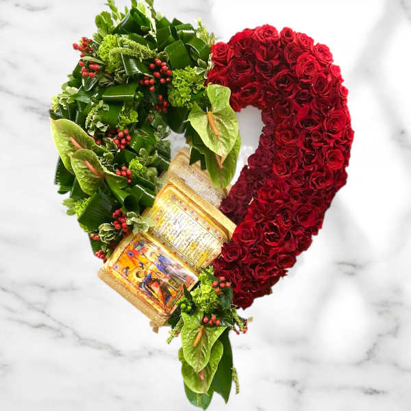 Heart-shaped floral arrangement of red roses and green tropical foliage with a religious book centerpiece