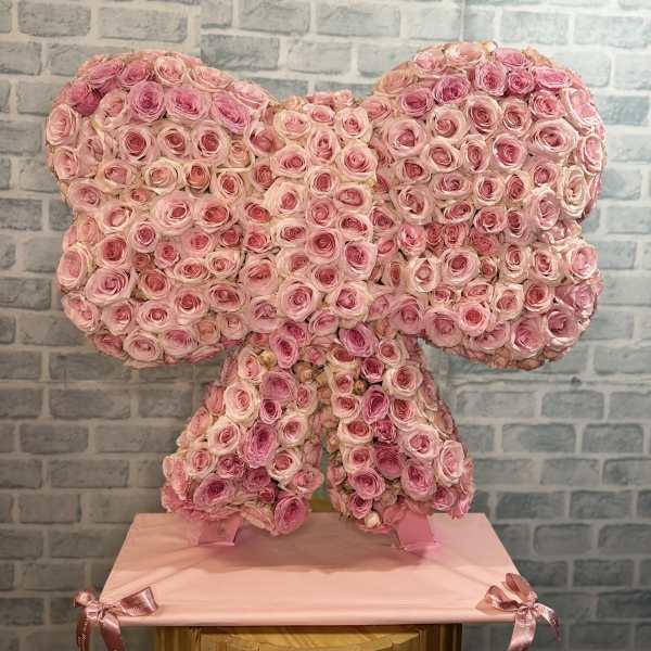 Pink rose arrangement shaped like a bow on a pedestal