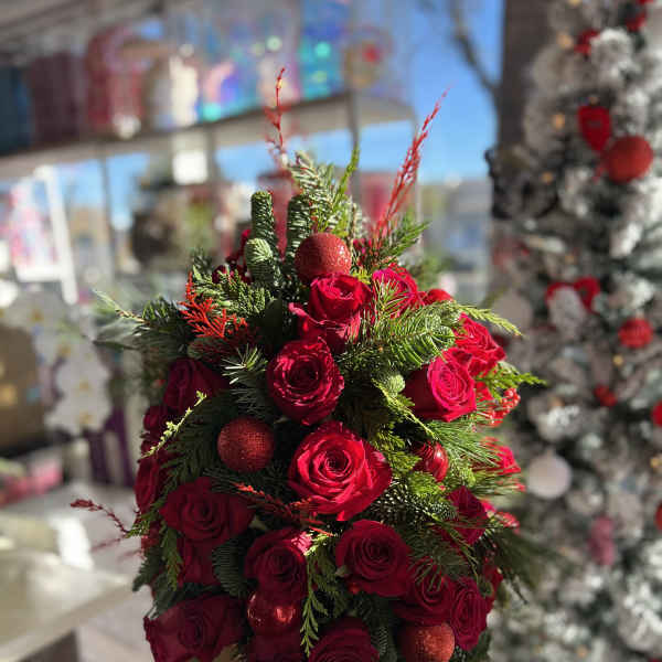 Red roses arranged with evergreen and red ornaments in a red container