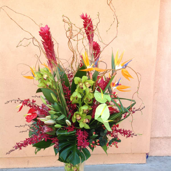 Tall tropical flower arrangement in a glass vase with red, green, and orange blooms