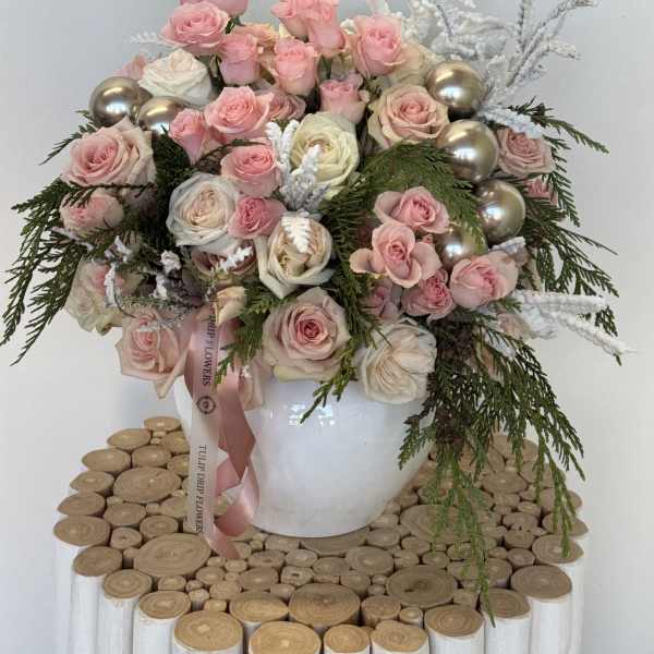 Pink and white roses arranged in a white vase with silver ornaments