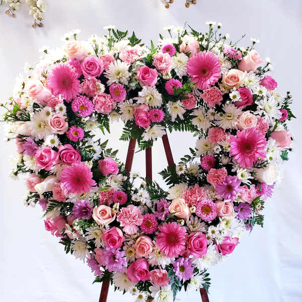 Heart-shaped floral wreath with pink roses and white daisies on an easel