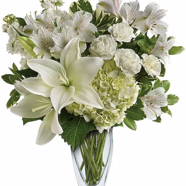 White lilies and mixed white flowers arranged in a clear glass vase
