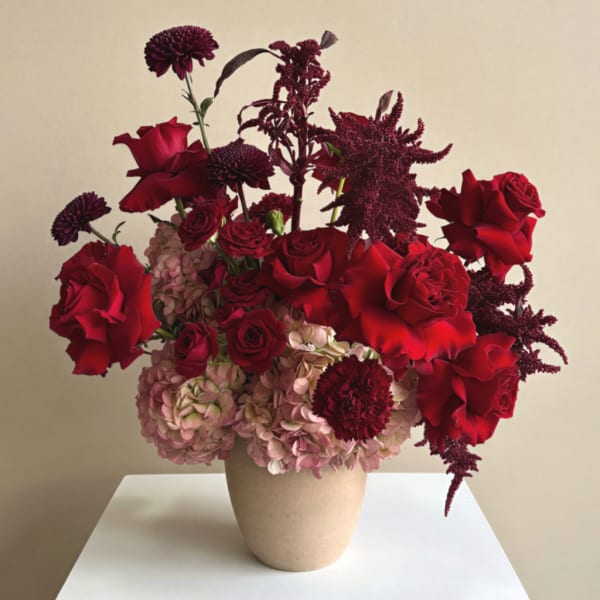 Red roses and burgundy flowers arranged in a beige vase