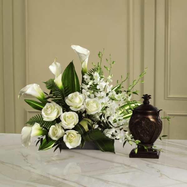 White roses and calla lilies arranged with white orchids in a low vase
