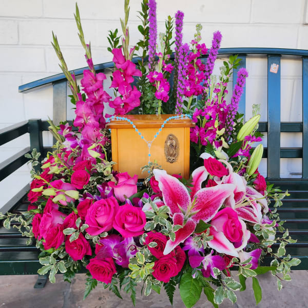 Pink floral arrangement around a wooden religious plaque on a bench